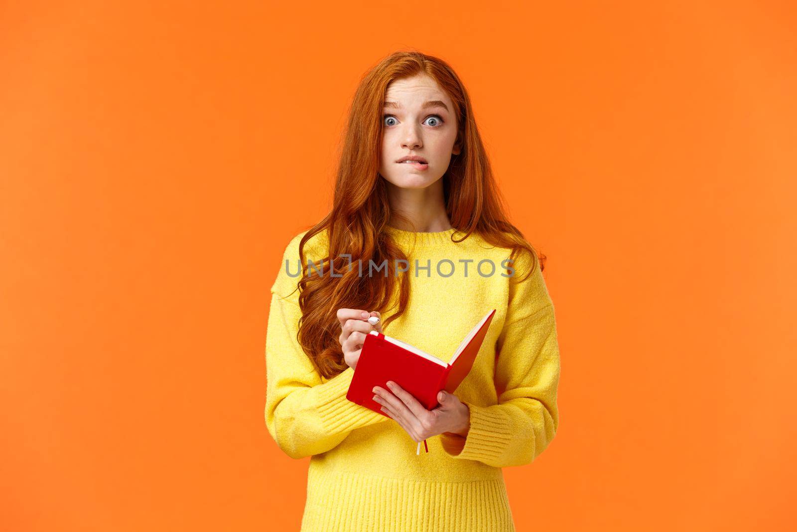 Troubled redhead caucasian girl forgot about appointment, remember task after looking notebook, biting lip and stare concerned or embarrassed, writing down important notes, orange wall by Benzoix