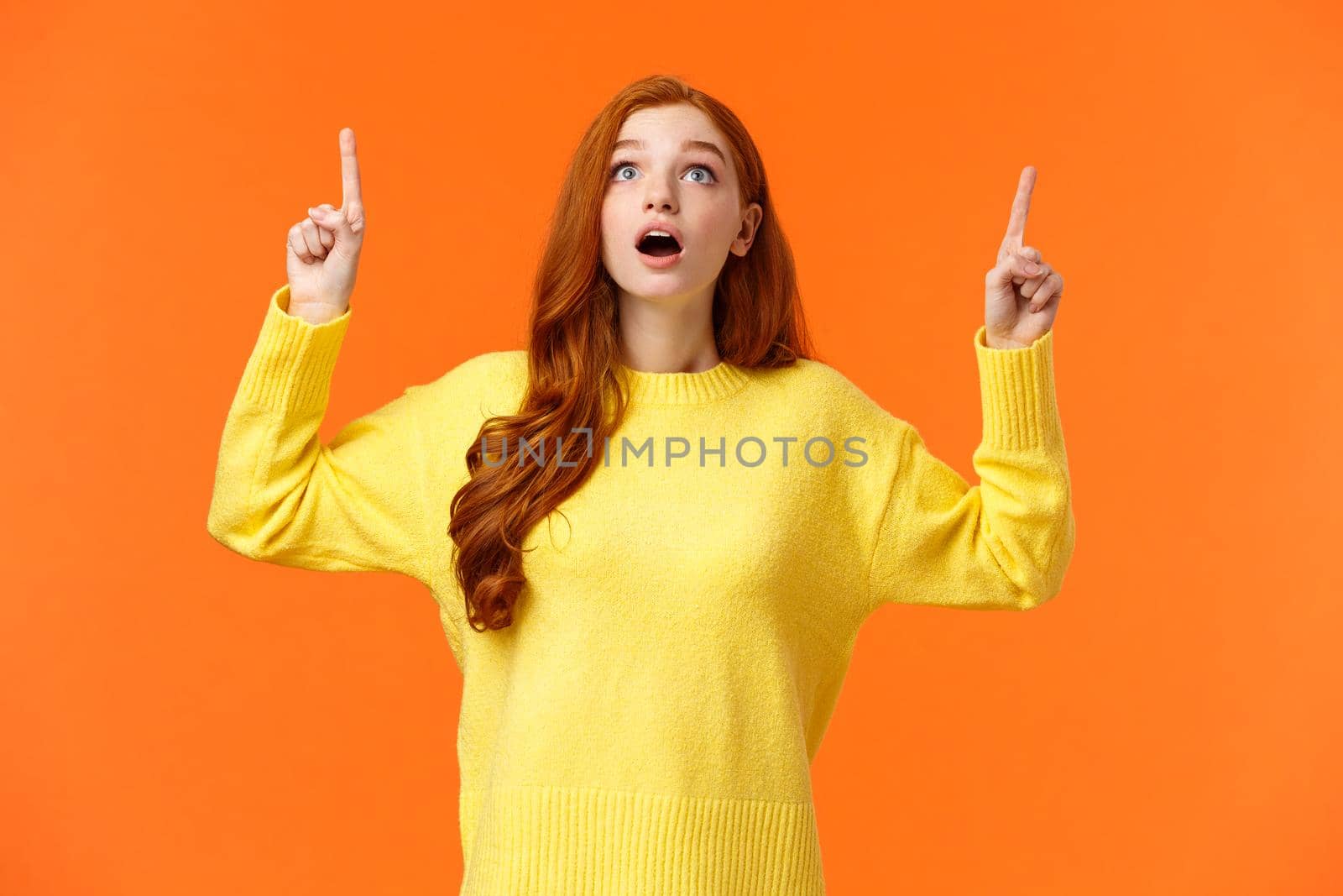 Excited, speechless and startled amazed redhead woman see awesome shopping sale promo, gaze and pointing up, stare top advertisement dropped jaw, breathtaking scenery, orange background by Benzoix
