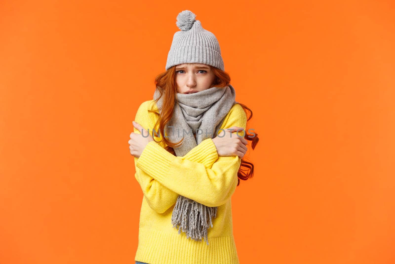 Sad cute redhead girl feeling discomfort, shaking from freezing cold, embracing own body get warm, frowning and grimacing unhappy, sulking, standing outside low temprature in hat and scarf by Benzoix