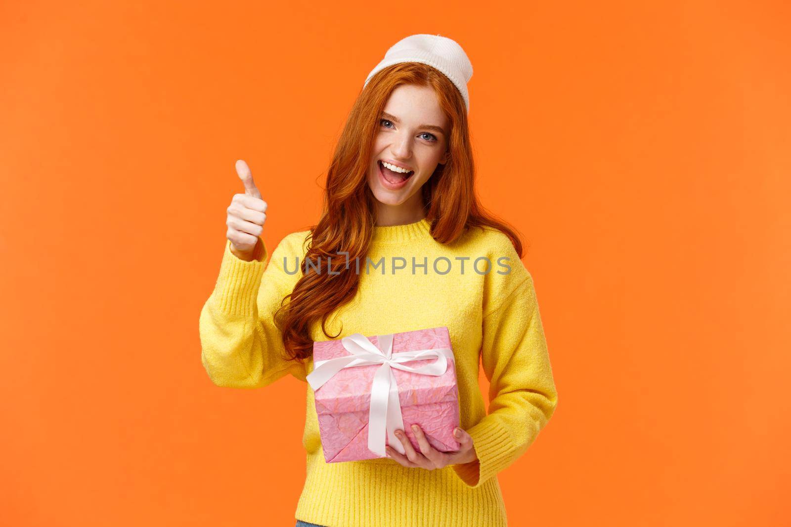 Girl enjoying holidays, got super cool present. Cheerful and upbeat good-looking redhead woman in yellow sweater, winter white beanie, show thumb-up in yes, approval or like gesture, smiling.