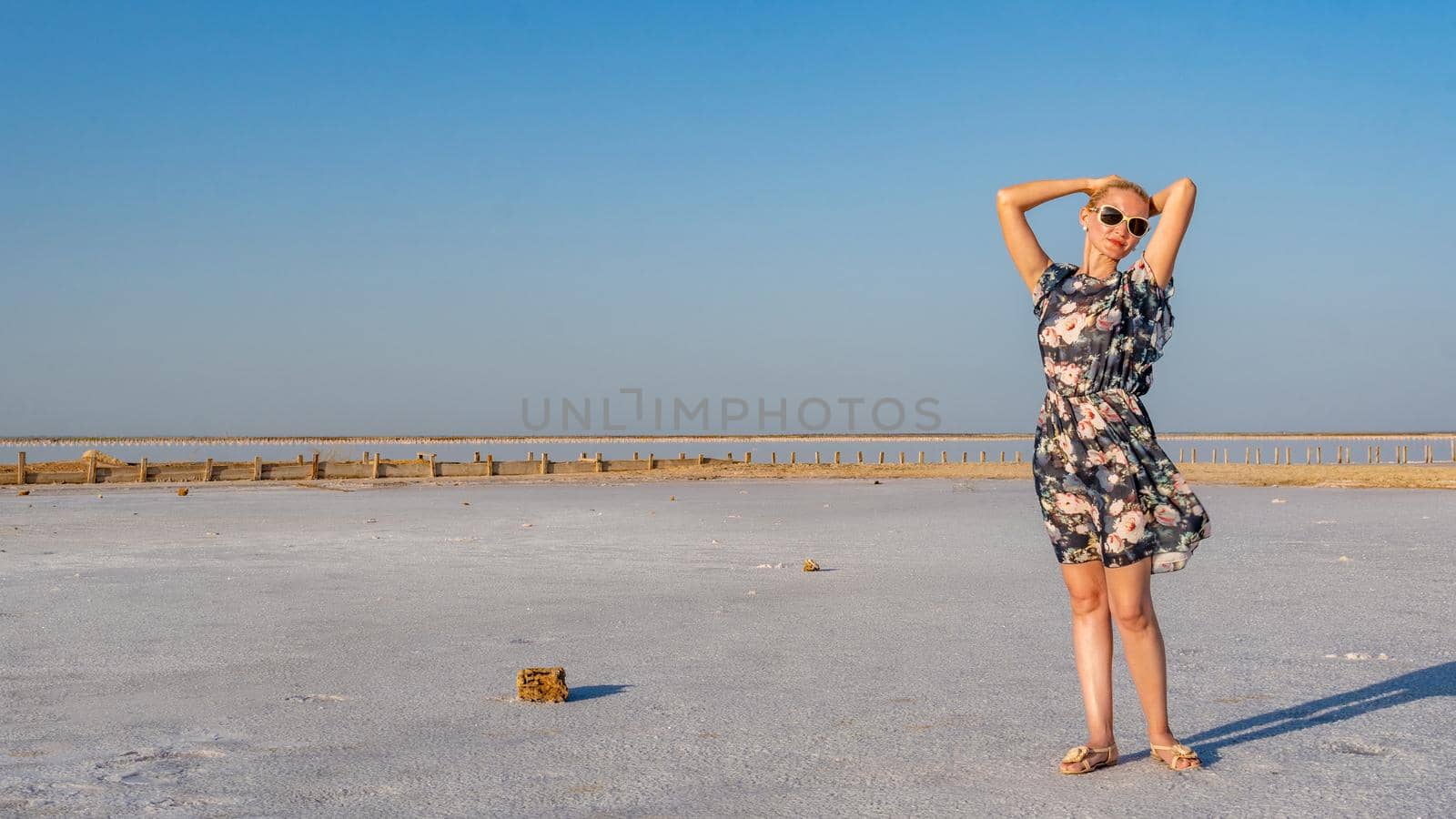 Cheerful girl in a beautiful dress with a kind look on a salty background like in winter on a lake with blue clouds in hot sunny weather by 89167702191