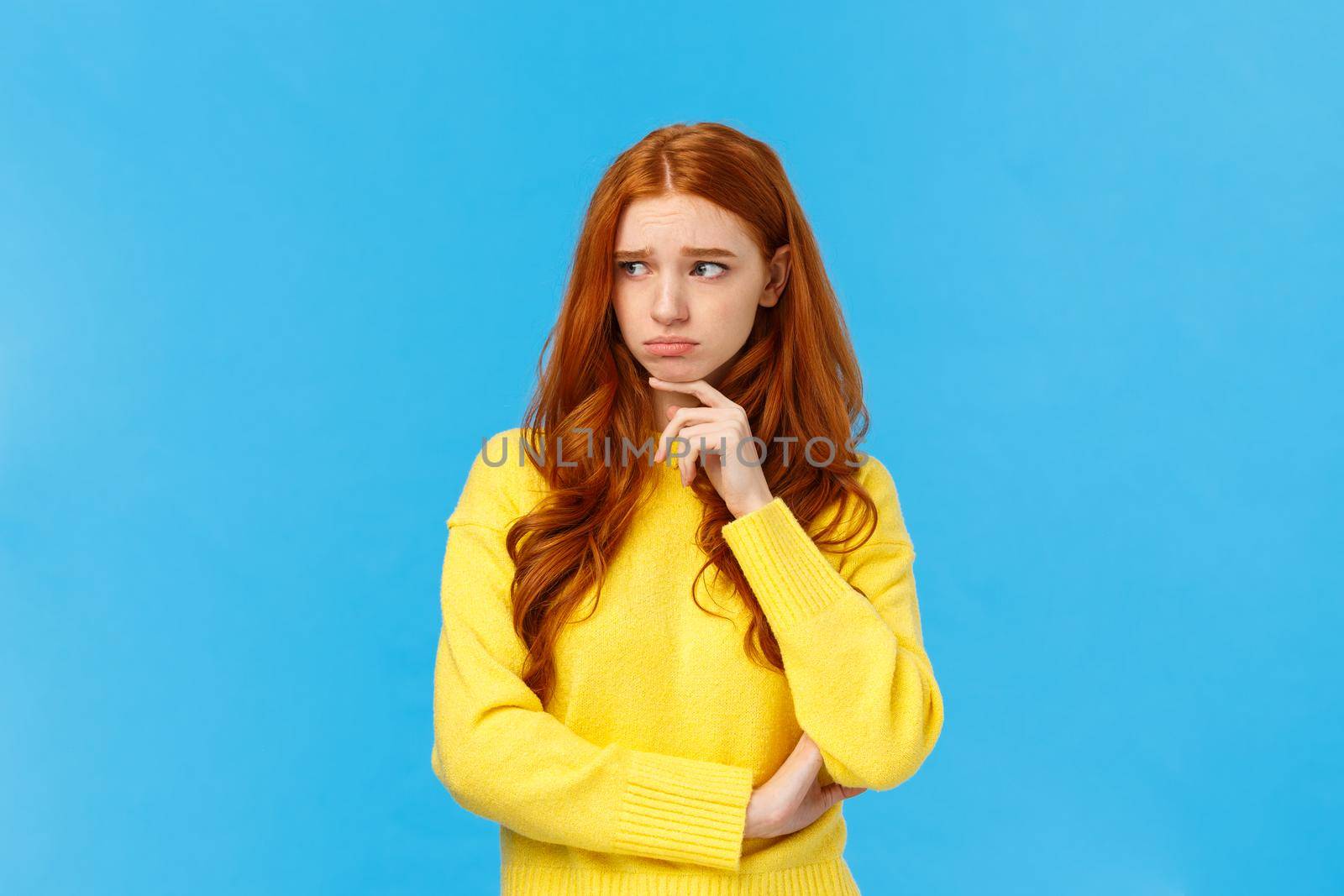 Sad timid and lonely redhead woman too feeling let down and depressed, sulking looking upset and envy left, frowning touching lip pensive, having bad feeling, standing anxious over blue background by Benzoix