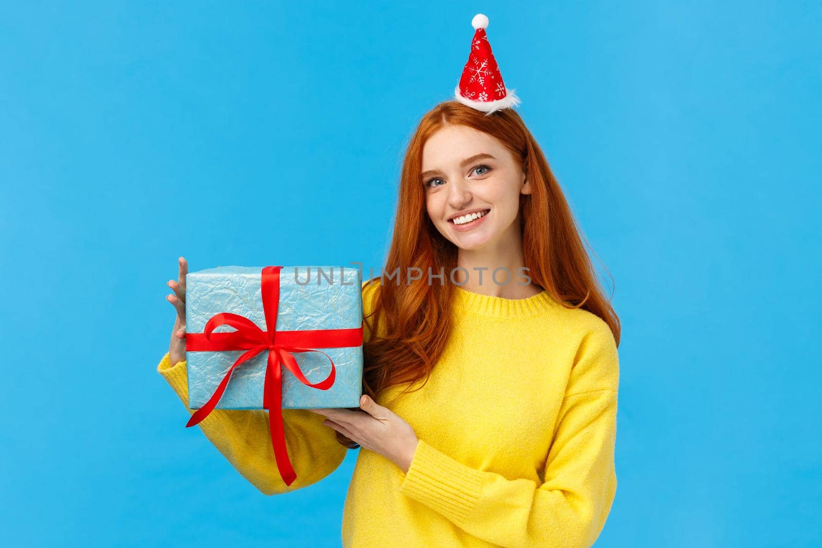Waist-up portrait young cute redhead caucasian female celebrating christmas holidays, new year party, exchanching gifts with friends during secret santa, holding box of present, wear fancy hat.