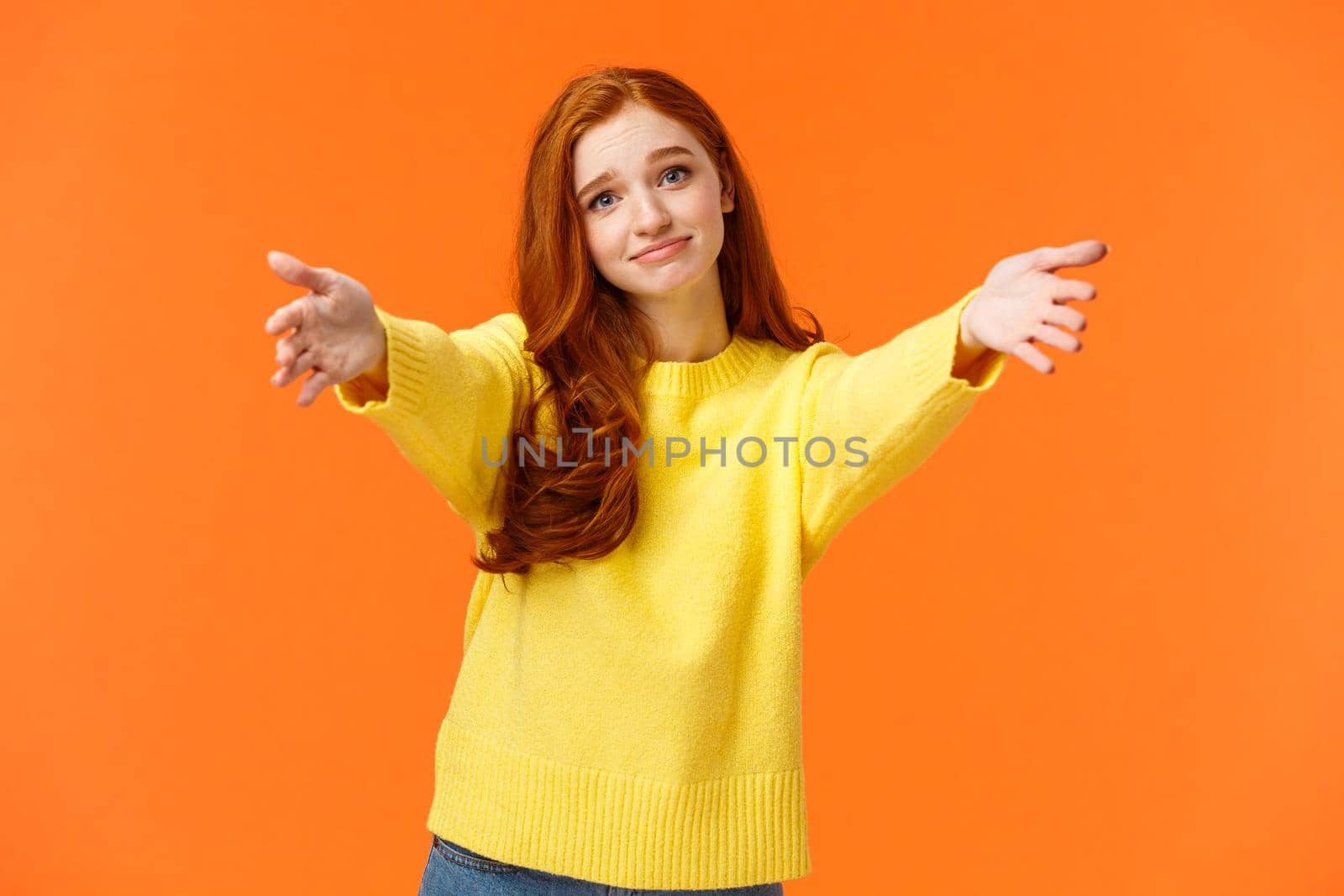 Girl asking come here to give cheer-up hug. Cute and touched tender redhead woman in yellow sweater, extend arms,stretch hands forward for cuddle, embrace friend, smiling lovely, orange background.
