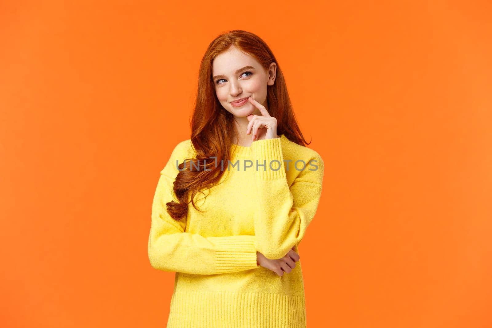 Mysterious and smart redhead creative girlfriend prepare perfect plan, look satisfied and sly upper right corner, smirk and touch jawline as thinking, have excellent idea, orange background.