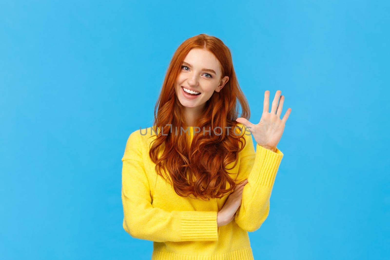 Cheerful, charismatic friendly redhead female showing high five, number fifth as making order, reservation or booking place for party, counting, standing blue background carefree in yellow sweater.