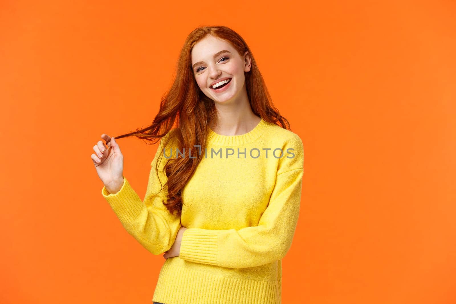 Carefree good-looking, smiling toothy redhead woman, girl with ginger hair laughing as chatting friends, rolling curl on hair, tilt head and smiling joyfully, having conversation, orange background.
