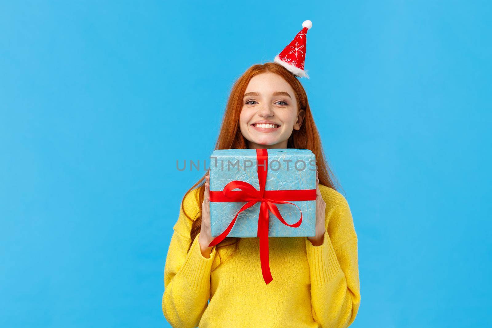 Excited and happy cute redhead girlfriend enjoy celebrating christmas, secret santa event as receive lots gifts, holding present, bragging with blue wrapped new year gift, smiling joyfully.