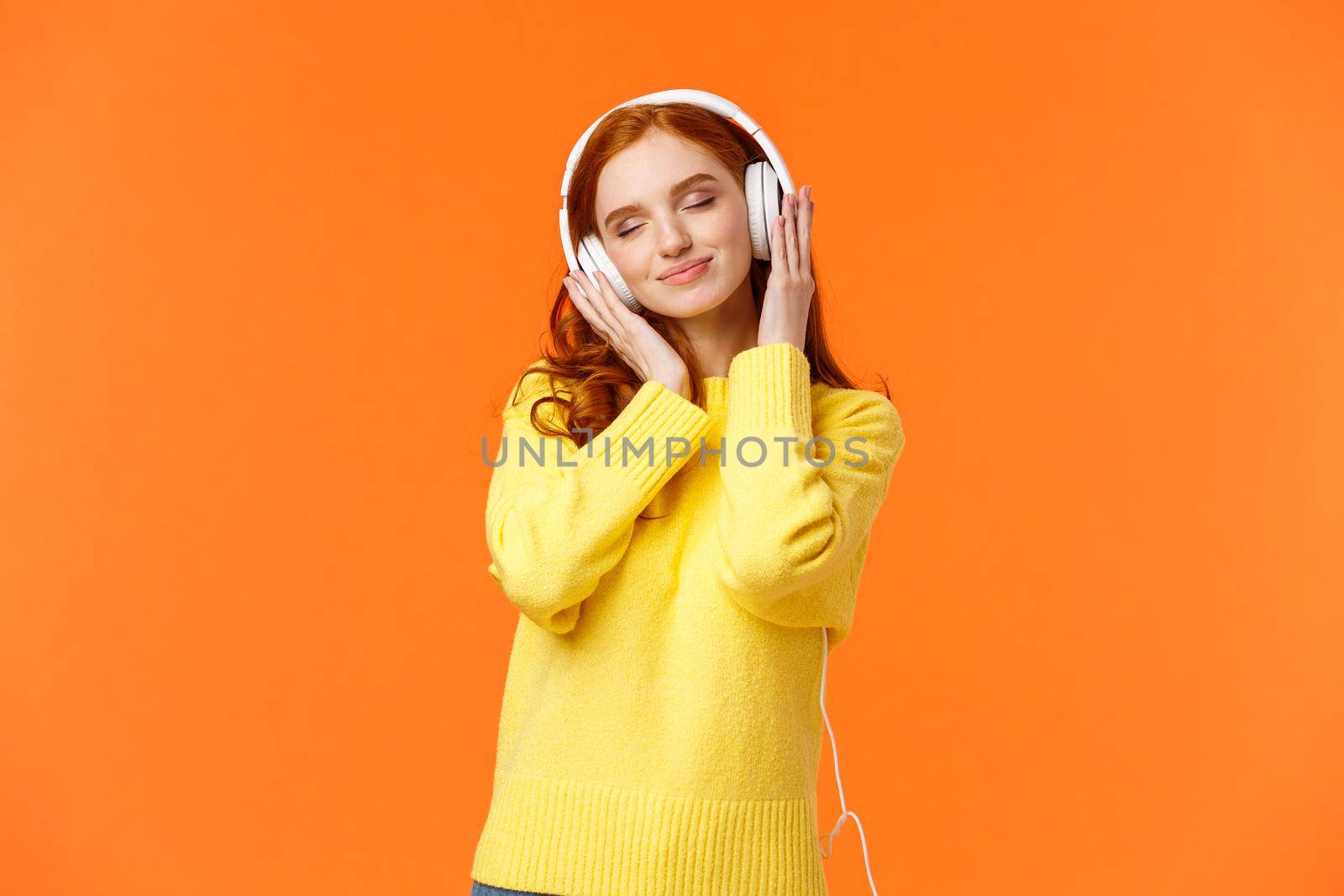 Girl enjoying nice soft sound of headphones. Cheerful romantic and delighted pretty redhead woman tilt head with closed eyes and tender smile, carried away with music in earphones.