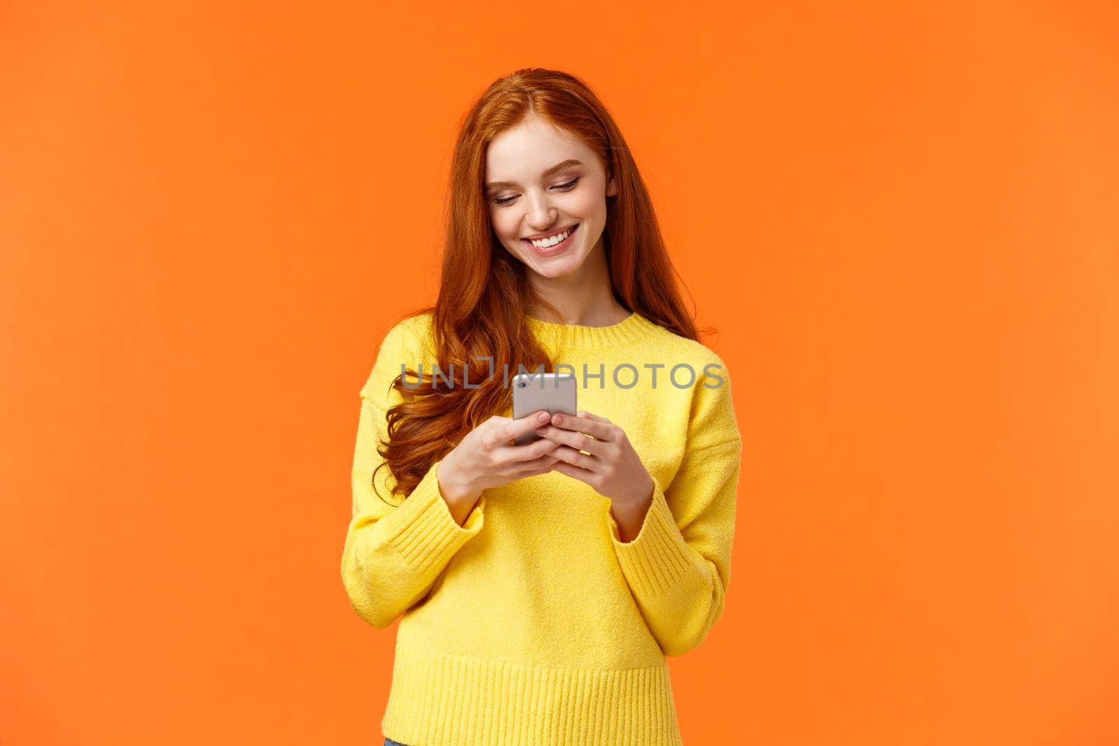 Communication, people and chat concept. Carefree modern hipster girl edit photos with filters on smartphone application, use app for chatting, smiling as looking mobile display, orange background.