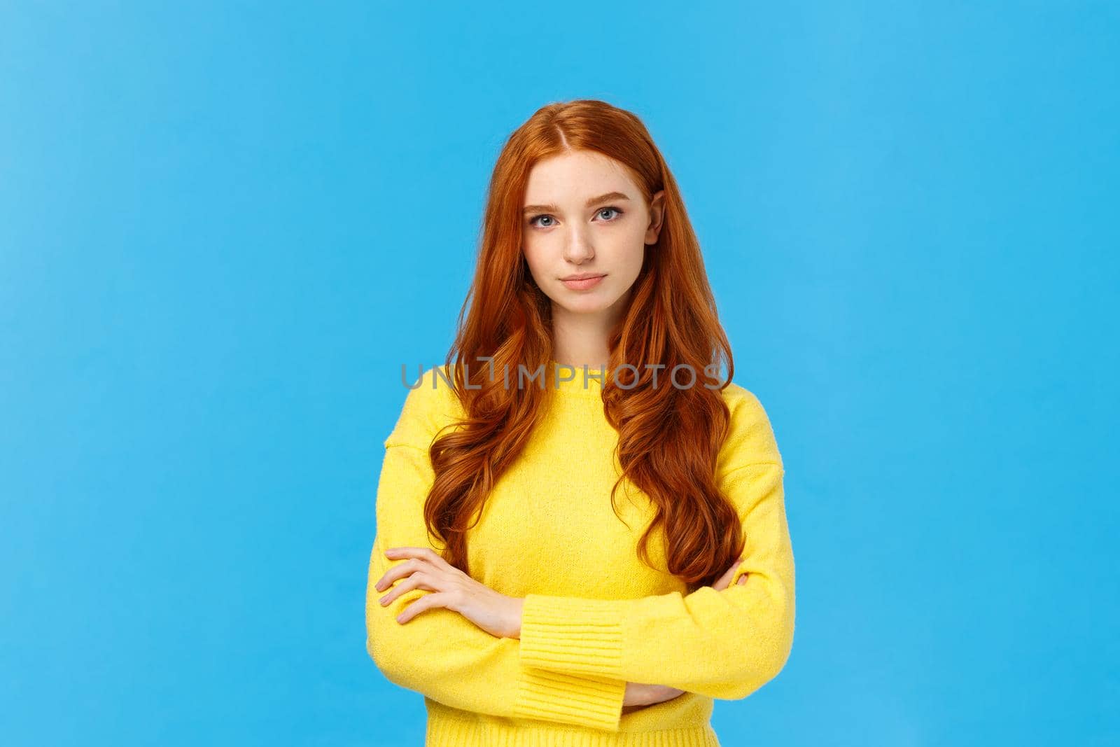 Professionalism, e-commerce and business concept. Serious-looking determined smart gorgeous redhead woman in yellow sweater, cross arms chest confident, looking camera, blue background.