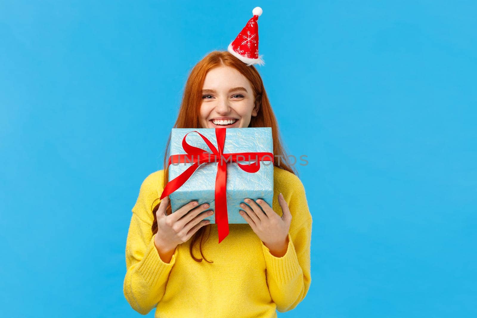 Girl cant wait give sibling her gift, smiling carry cute christmas wrapped present and wearing fancy santa hat, laughing, sharing positive emotions, attend winter holidays party, blue background.