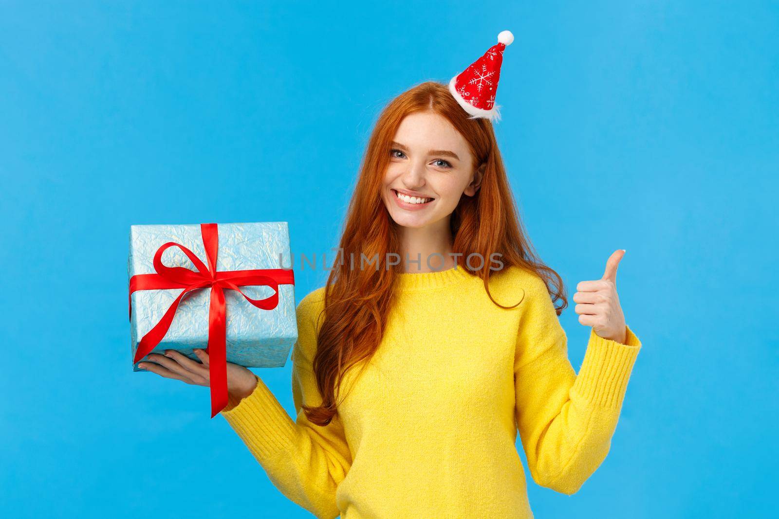 Waist-up shot satisfied good-looking redhead woman showing thumb-up in approval or like, love celebrating christmas holidays and receive gifts, holding bix box of present and wear fancy hat, smiling.