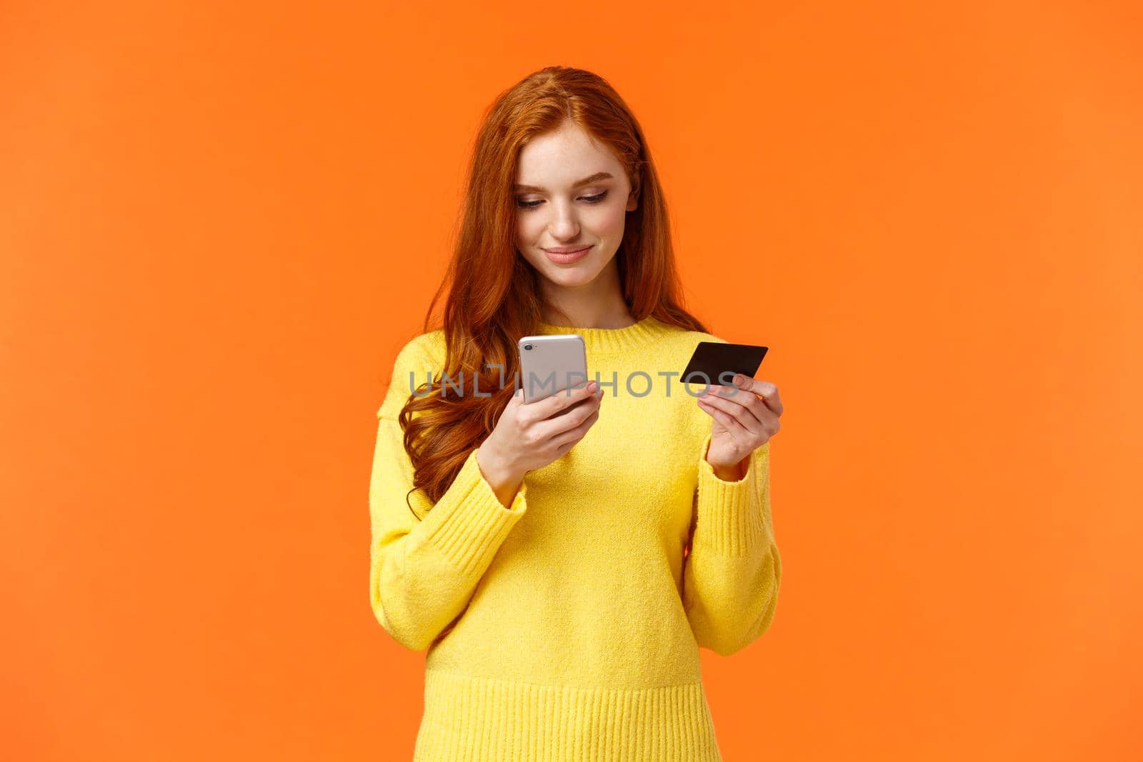 Waist-up portrait carefree modern young girl making online purchase, shopping internet using mobile application, insert credit card info smartphone, smiling, order something, orange background by Benzoix