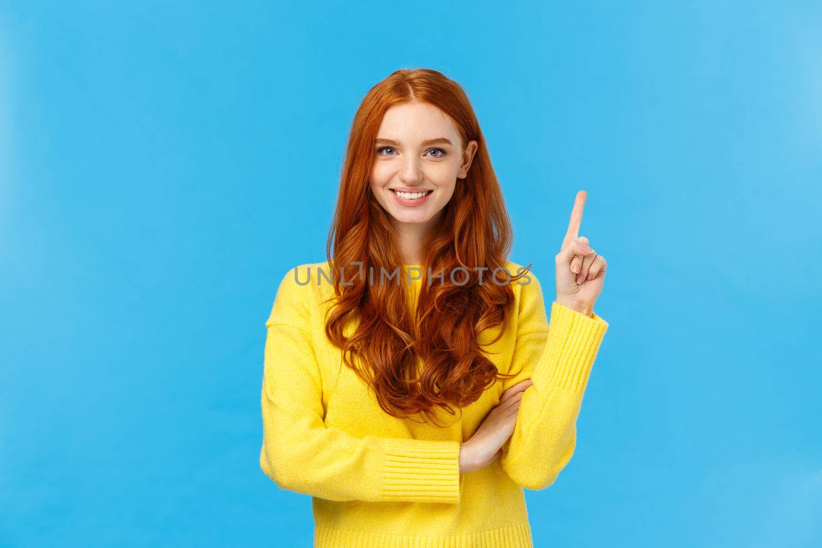 Attractive confident and charismatic caucasian redhead female in yellow sweater, showing number one, order product, being first, smiling satisfied and assertive, standing blue background by Benzoix