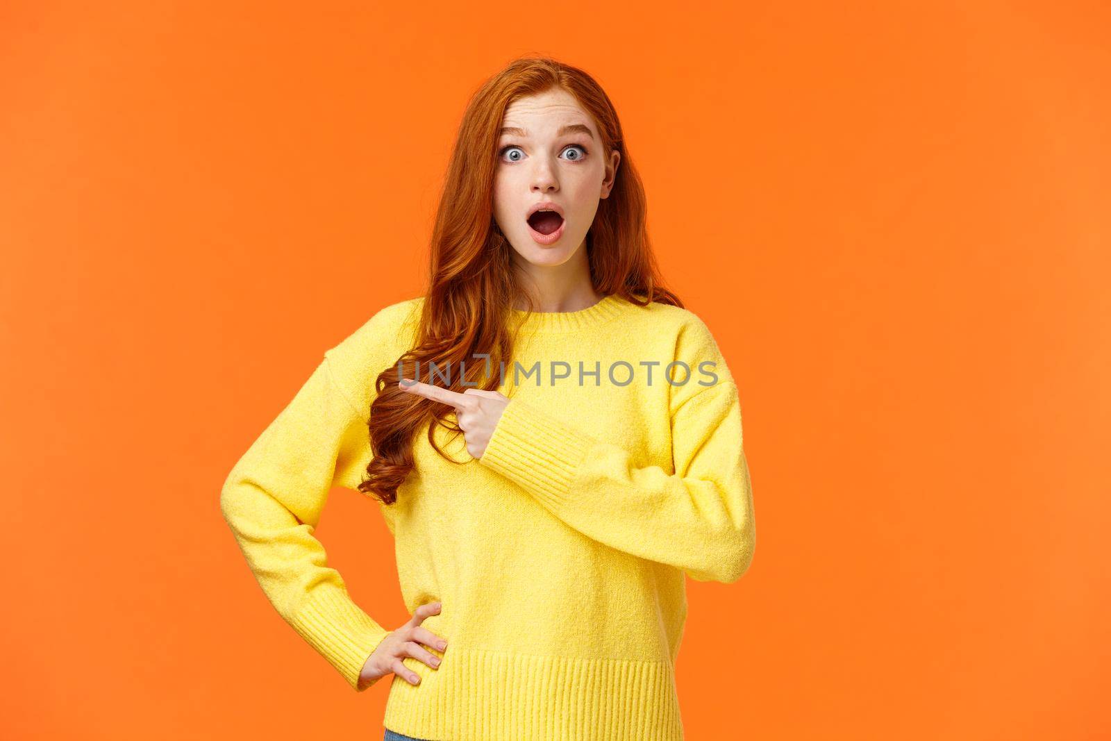 Speechless and impressed gorgeous fashionable redhead girl, young modern woman red hair, drop jaw, gasping astonished, stare camera and pointing left at interesting, awesome product by Benzoix