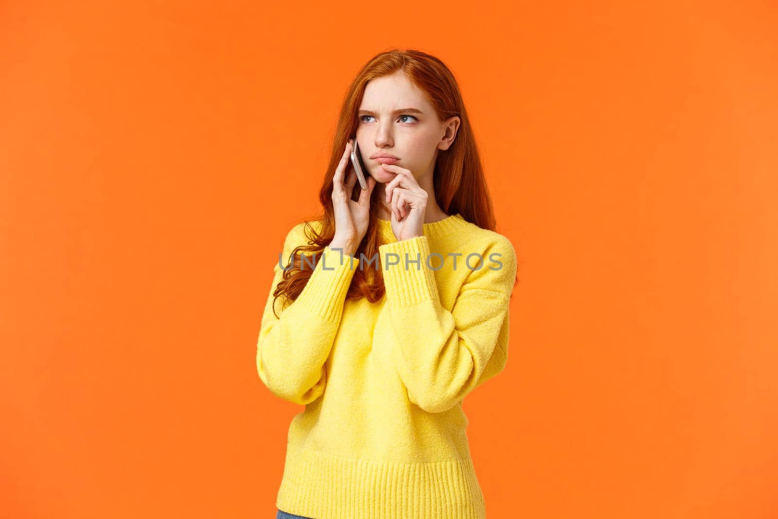 Indecisive and unsure, skeptical serious-looking redhead woman having tough decision make during conversation on phone, frowning touch lip pensive, order food delivery, orange background by Benzoix