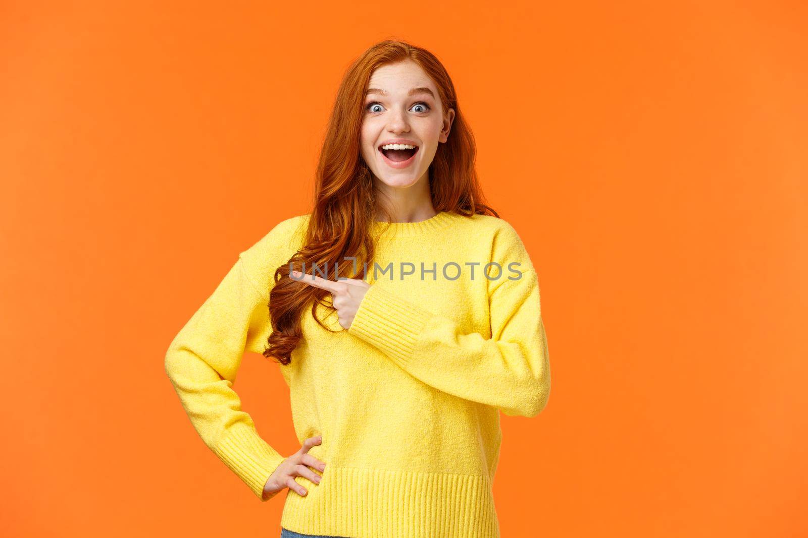 Happy, upbeat and dreamy cute redhead woman got chance travel abroad, telling about awesome company, promoting product on sale, stare fascinated camera smiling and pointing left, orange background by Benzoix