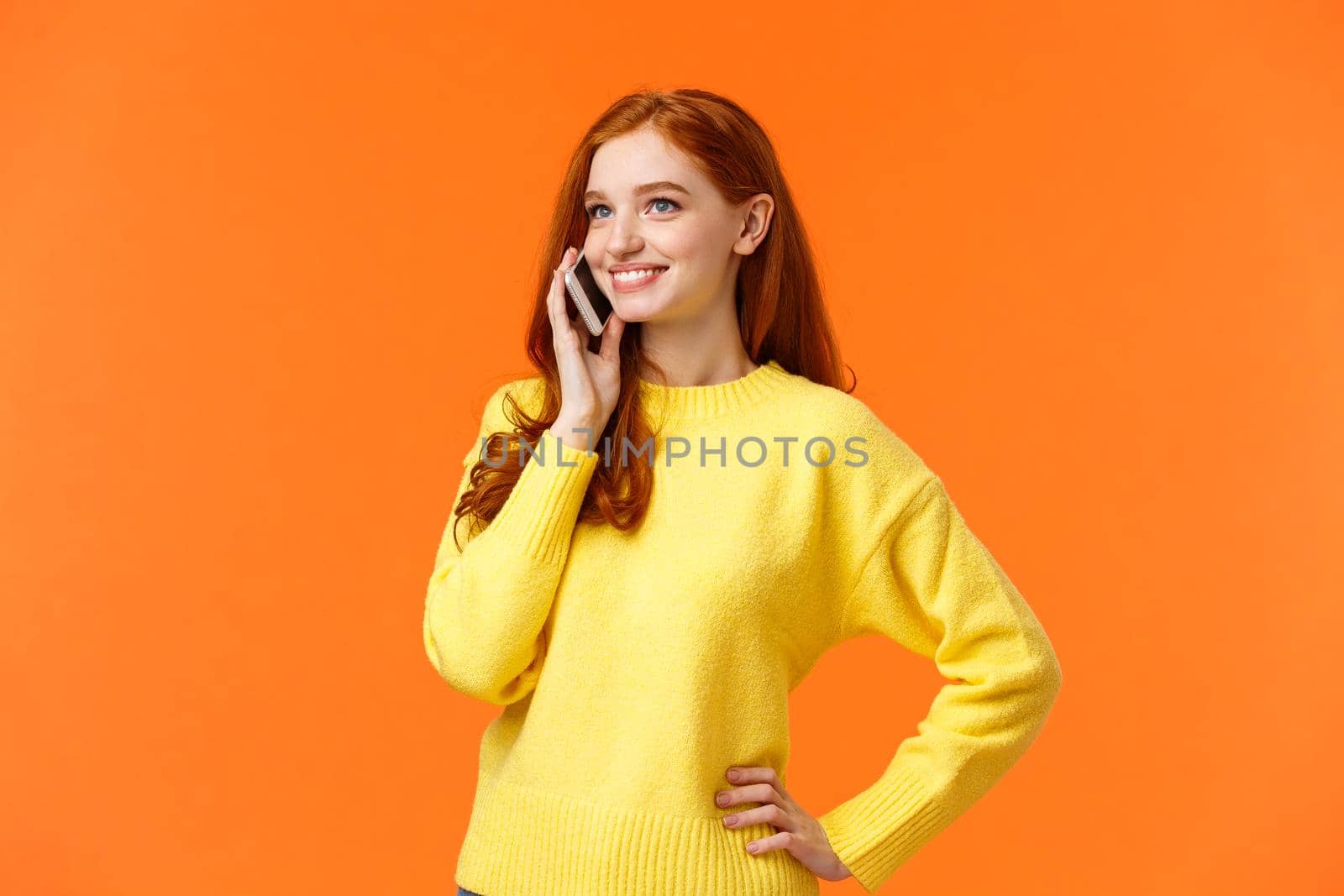 Waist-up portrait pretty redhead female calling friend, having conversation, confirm online order while shopping for holidays, standing carefree hold smartphone near ear, orange background.