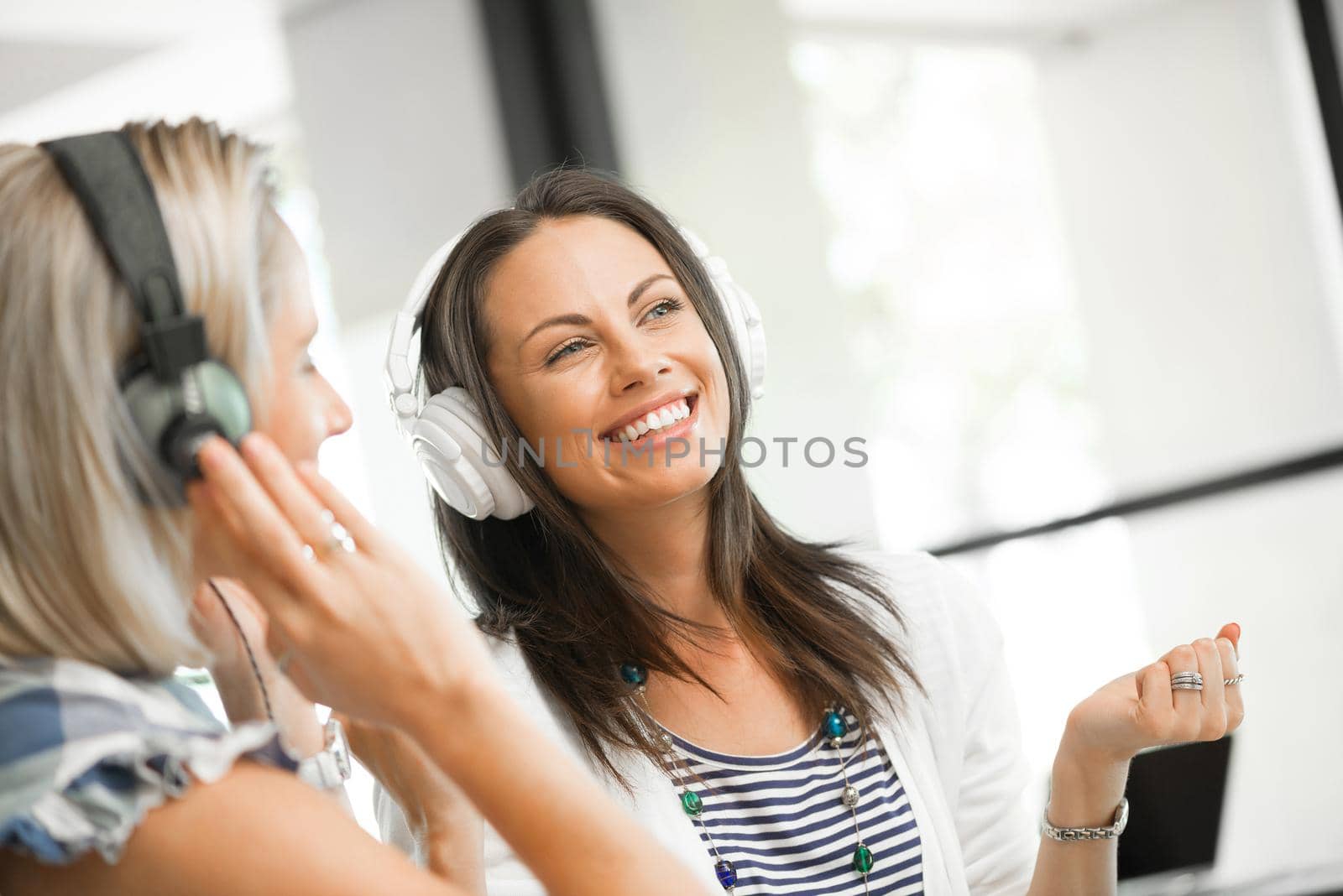 Two pretty women in headphones sitting at desk in office