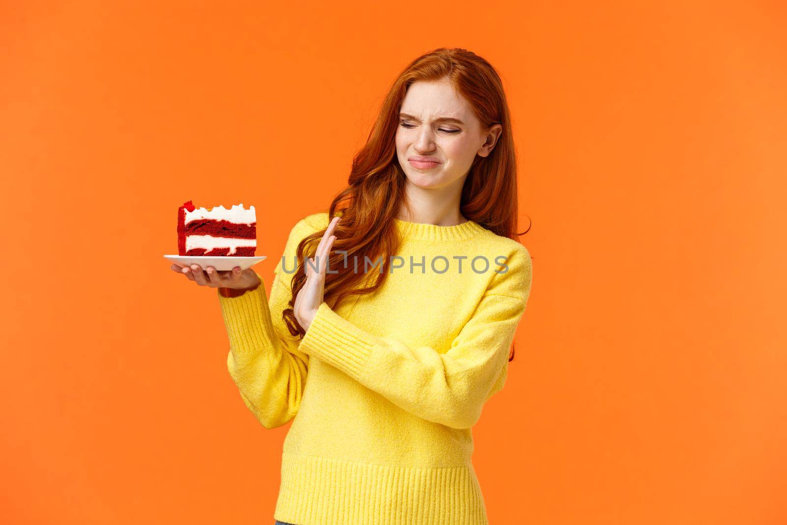 No thanks, dont want. Cute redhead girl trying resist temptation take bite delicious sweets, holding tasty cake and showing stop, refusal or rejection with grimacing face, express aversion, dislike.