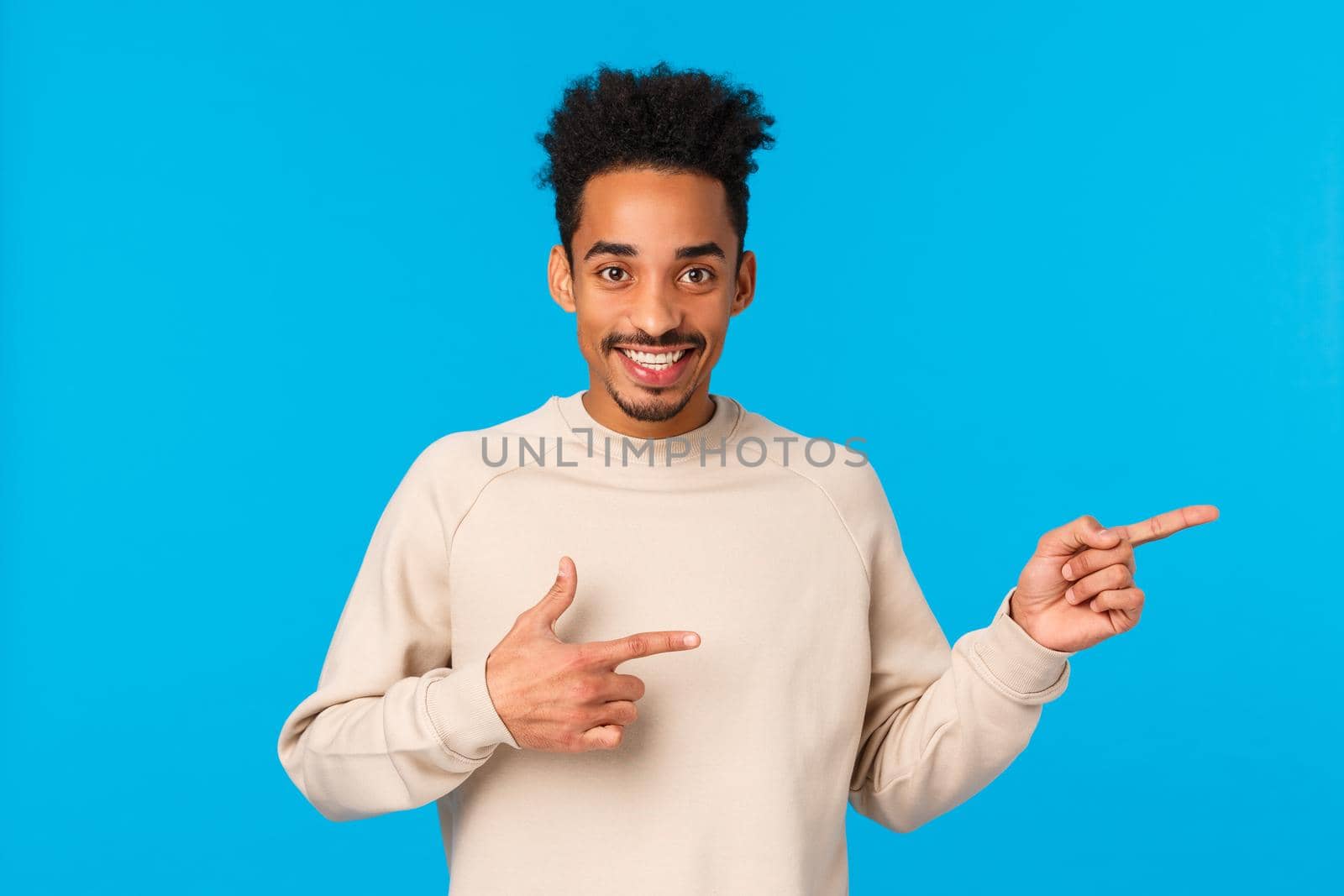 Advertising, technology and people concept. Modern hipster african american guy inviting join his company, telling about promotion, pointing right and smiling, recommend product, blue background.