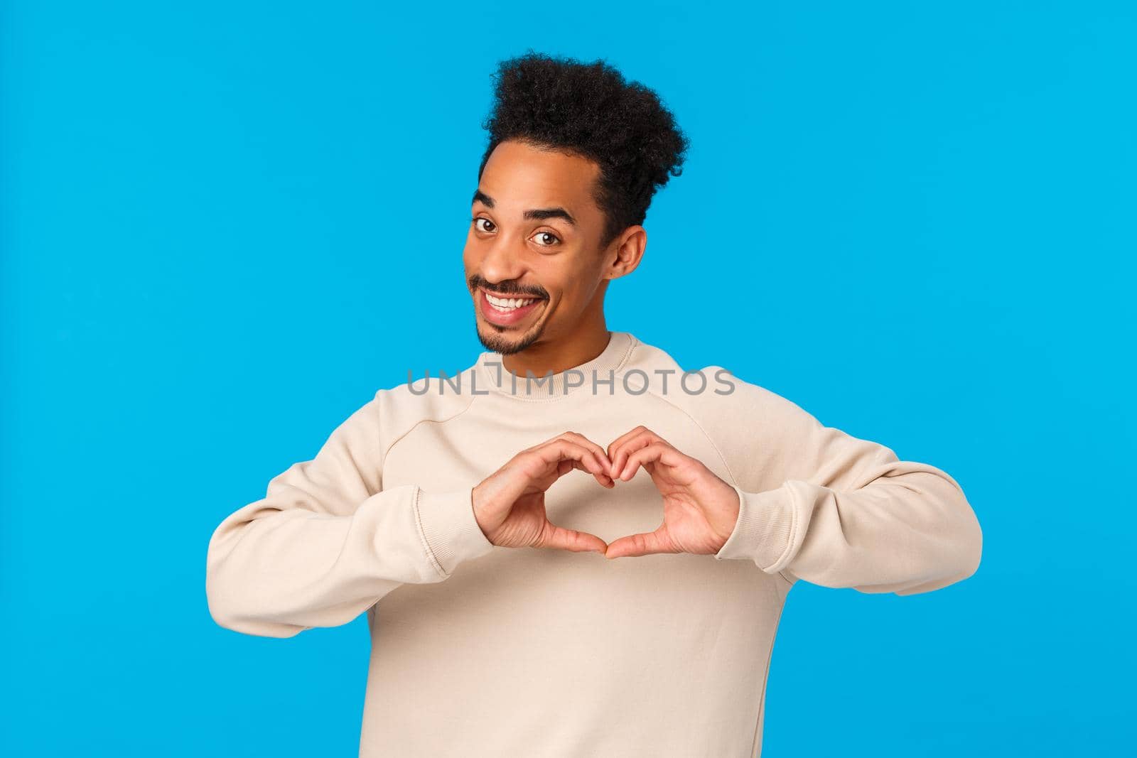 I love you. Cheerful and cute enthusiastic african-american smiling boyfriend making heart hands gesture near chest and grinning camera, make confession on valentines day, blue background.