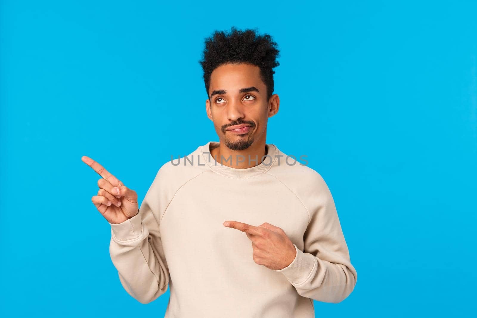 Skeptical and disappointed handsome stylish african-american modern guy in white sweater, smirk and staring with judgement and dislike at something lame, pointing upper left corner, blue background by Benzoix