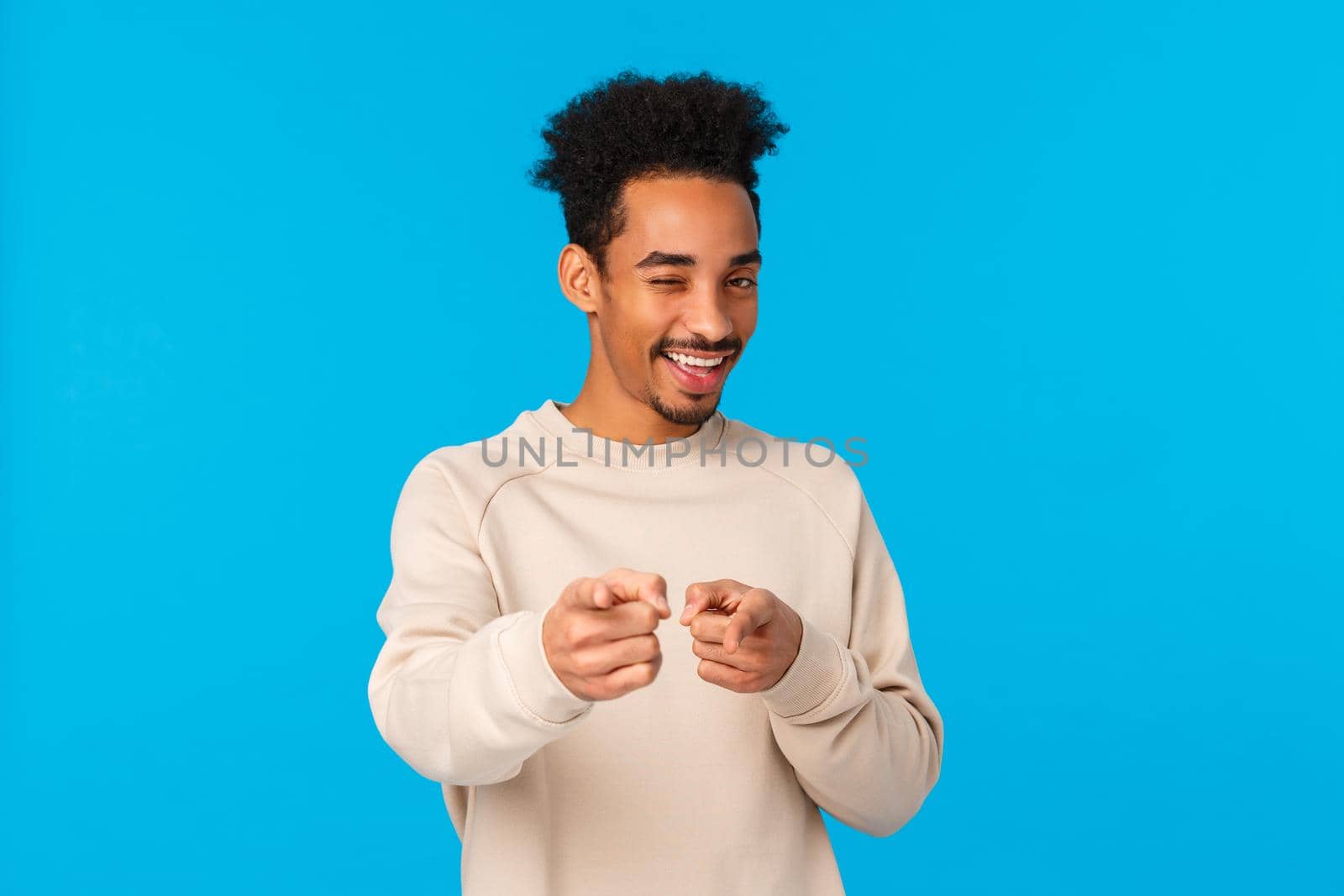 You rock, congratulations. Sassy good-looking african american hipster guy pointing fingers at camera and winking as choosing, indicating at winner or lucky person who achieved goal, blue background.