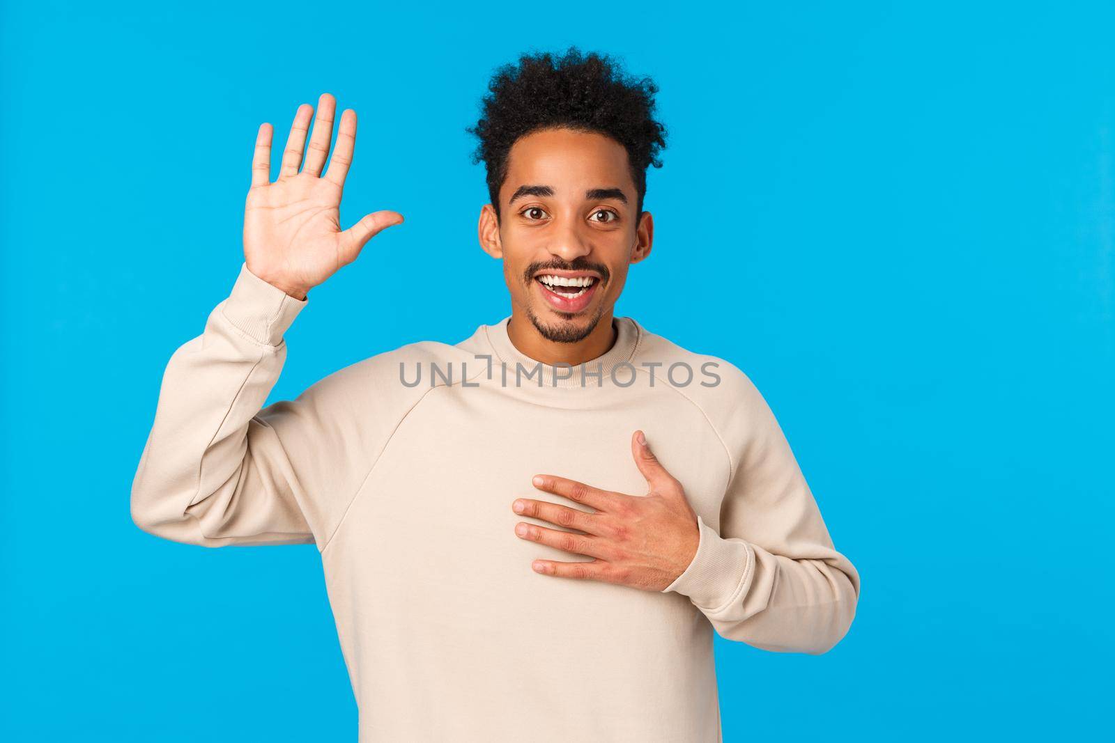 Friendly happy and attractive guy introduce himself, hold palm on heart and raise one hand, make promise, telling truth, being sincere as confess love or affection, smiling standing blue background by Benzoix