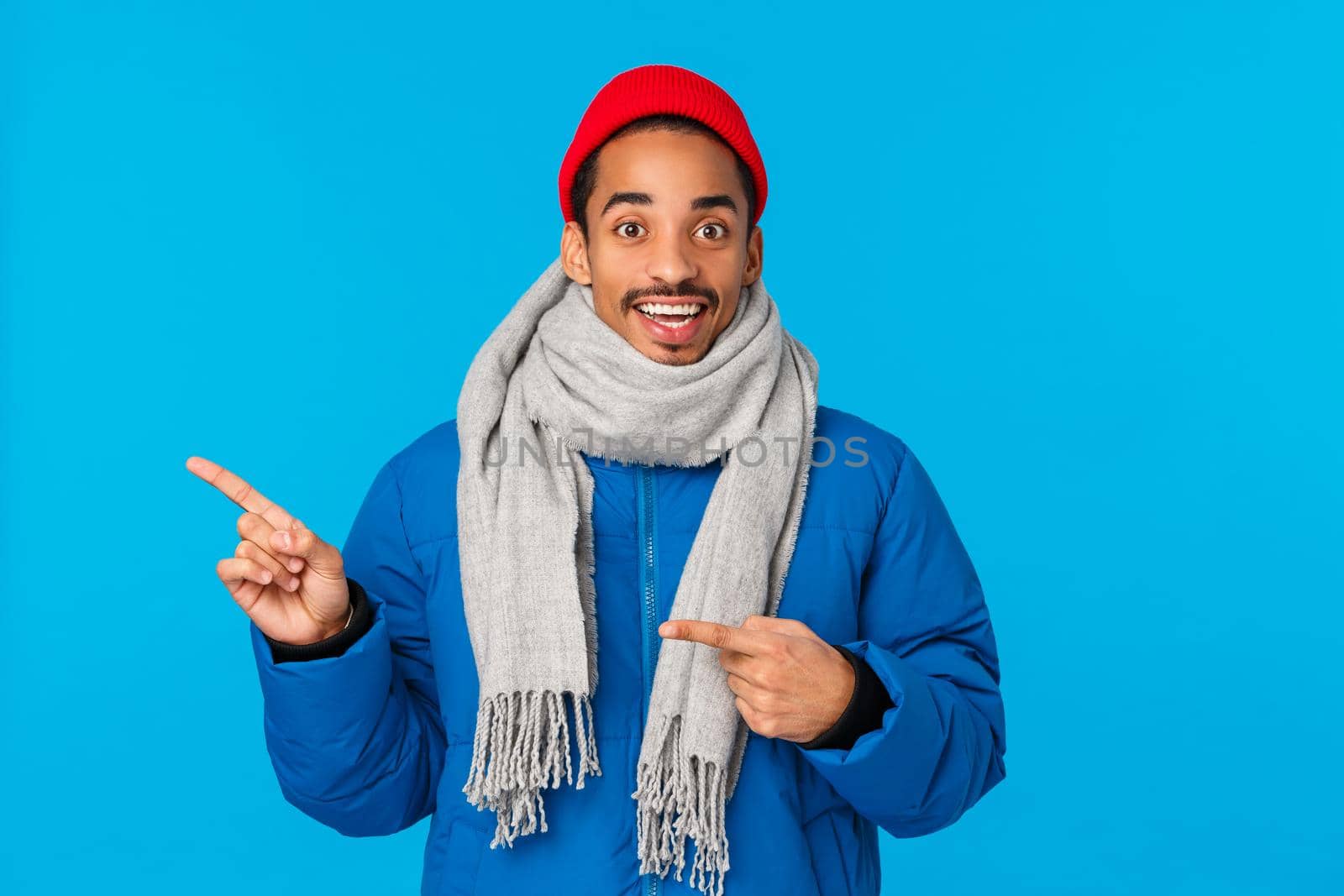 Amused and happy, entertained smiling young african american man showing awesome holiday event, telling cool advertisement info, pointing left inviting come together, wear winter clothes.