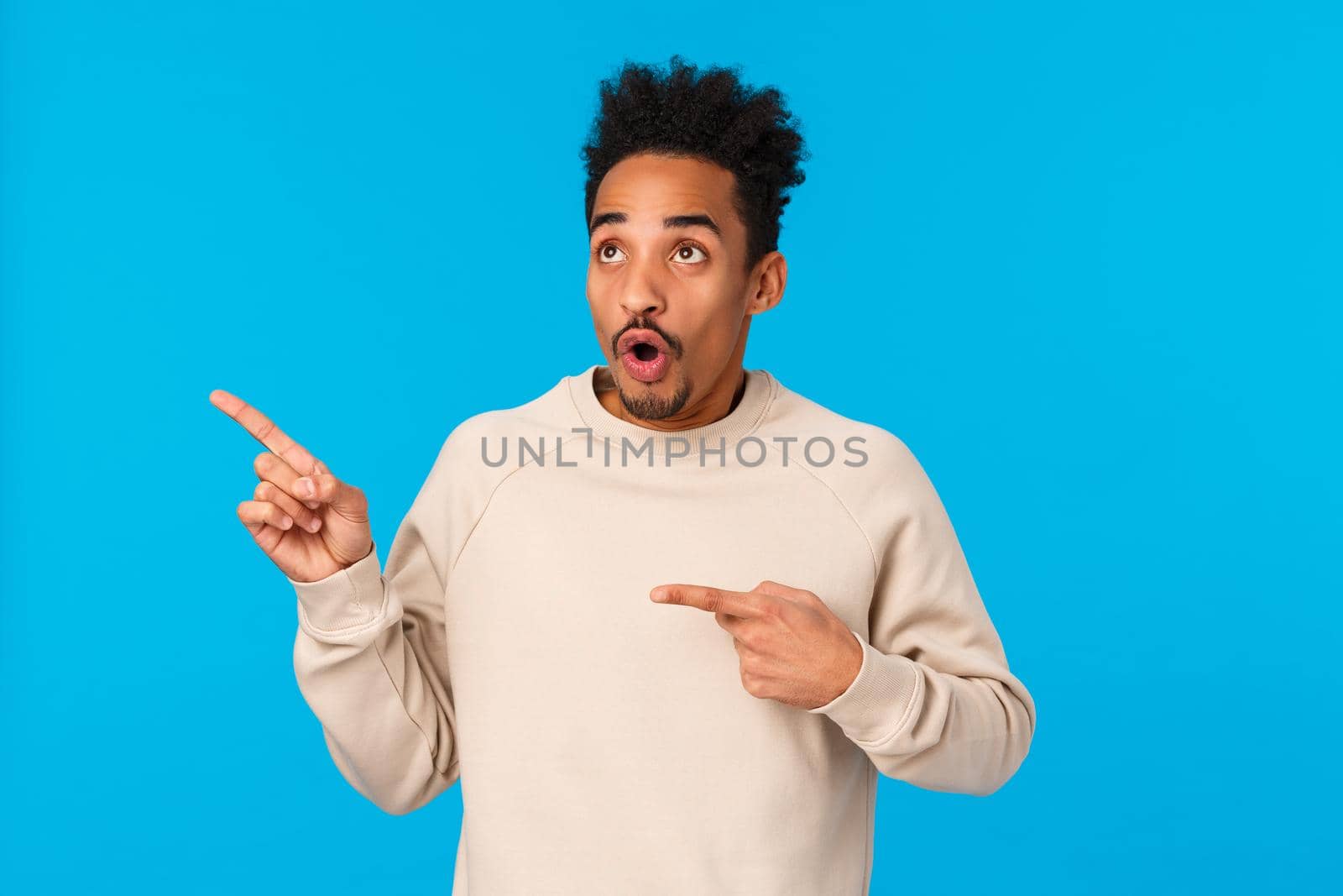Speechless and impressed, startled attractive african-american boyfriend seeing just what he need, losing speech standing blue background, open mouth staring upper left corner amazed.