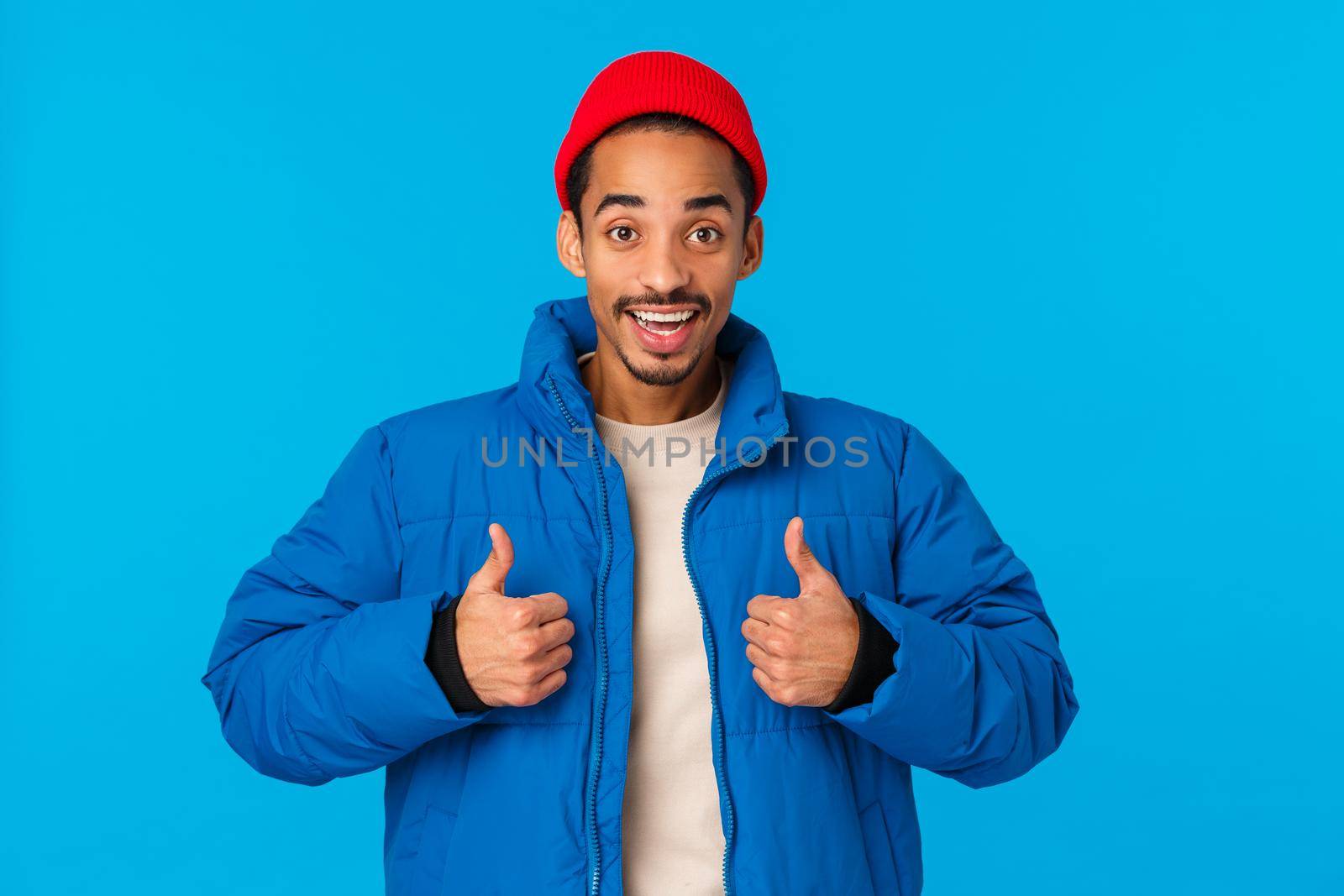 Man feeling alright, satisfied with new padded jacket mom bought christmas gift. Cute african-american satisfied guy in beanie and outdoor winter outfit, showing thumbs-up smiling in approval.