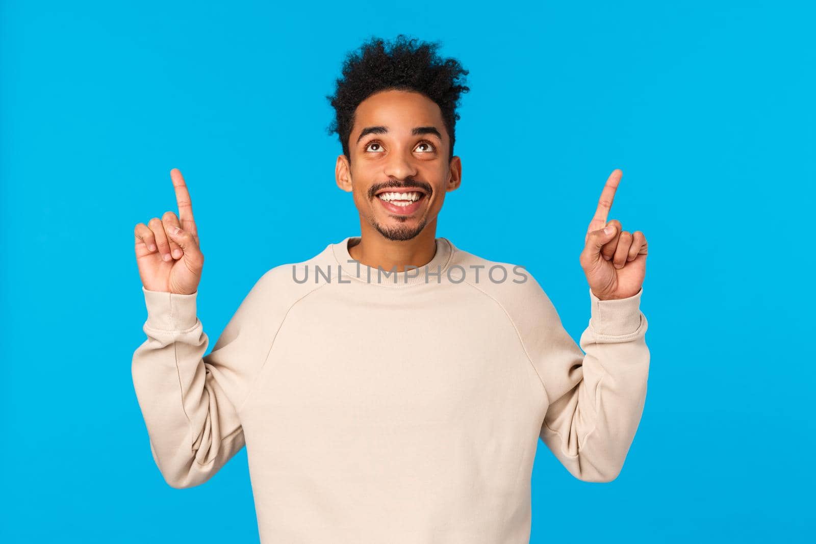 Wonderful promo. Amazed, excited smiling happy african american man with afro hipster haircut, moustache, looking pointing up admiring view, found excellent gift for valentines day, blue background by Benzoix