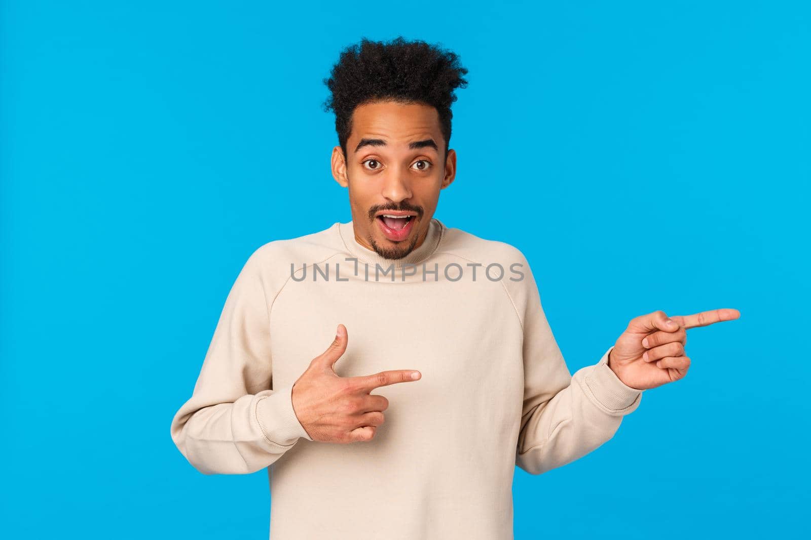 Excited and amused handsome guy visit awesome place, invite you participate, join company, pointing right to promote product, asking your opinion, making choice consulting friend, blue background.