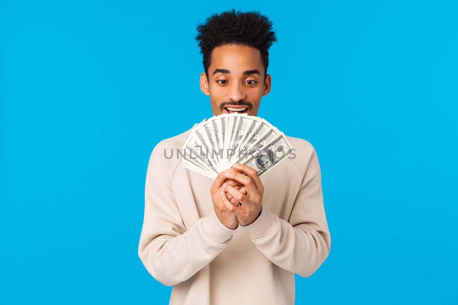 Money always sunny. Excited and happy african-american guy looking at cash with temptation and delight, dreaming what buy as winning lottery, got raise, standing blue background. Copy space
