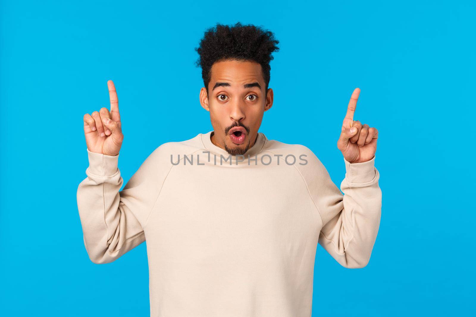 Have you seen it. Attractive impressed african-american guy with moustache, afro haircut, saying wow, telling about event, product advertising, pointing fingers up over blue background.