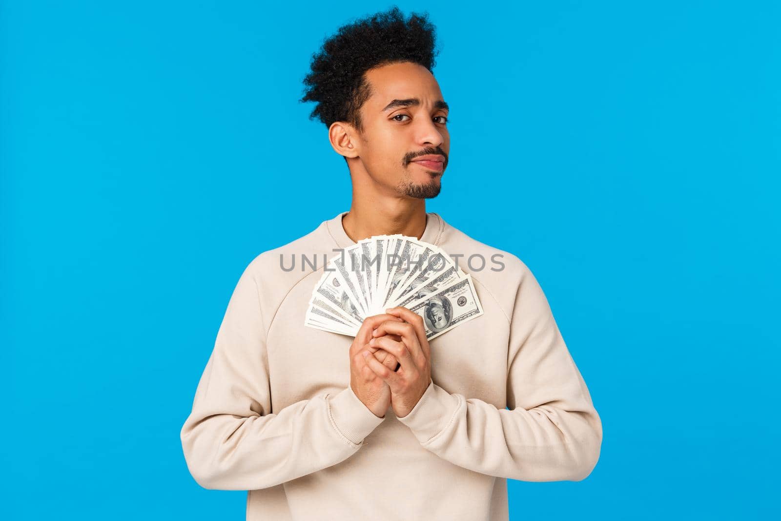 Suspicious and doubtful young pensive african-american rich guy holding big cash, lottery prize, have money and looking with disbelief or skeptical camera, unwilling share, standing blue background by Benzoix