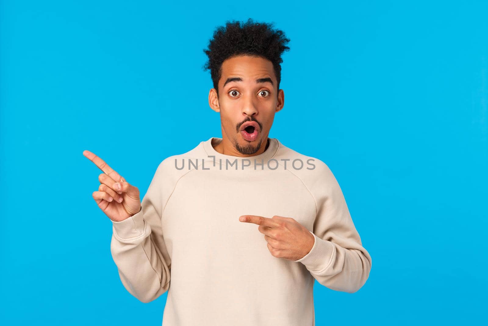 Wow amazing. Impressed and astonished, speechless attractive african-american with afro haircut, hipster guy pointing upper left corner, folding lips and gasping from breathtaking awesome event.