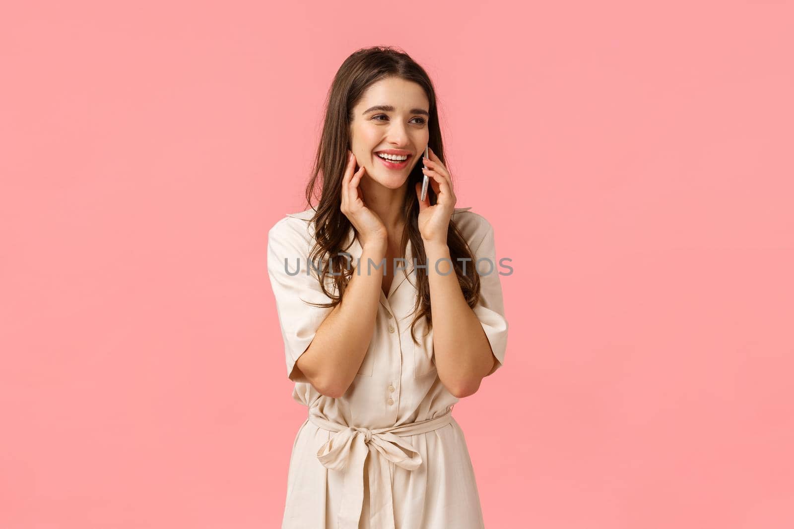 Cheerful alluring and carefree happy woman in dress, laughing talking on phone, calling best friend and discuss romantic date, holding smartphone near ear, look sideways, pink background by Benzoix