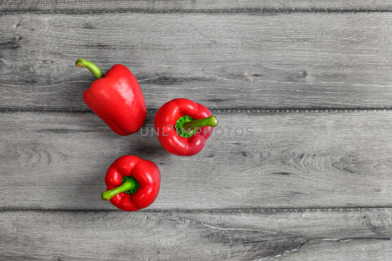 Tabletop view - three bright red bell peppers on gray wood desk