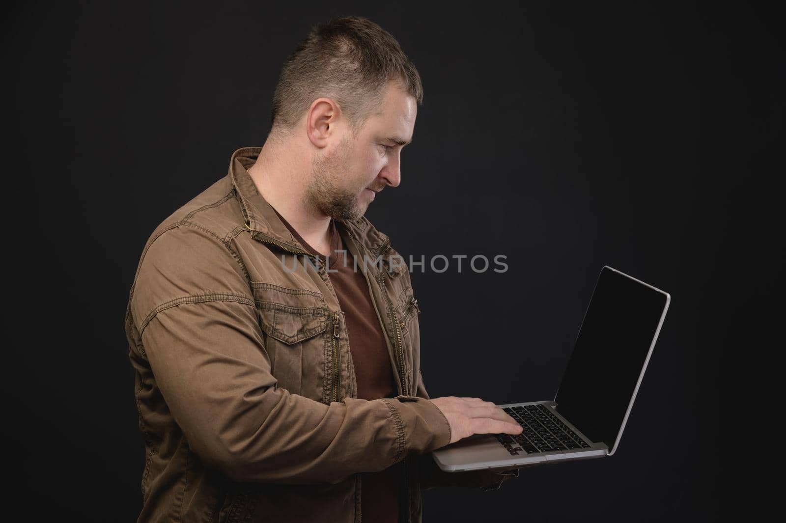 Middle aged Caucasian man uses laptop while standing in studio. Portrait of a freelancer surfing the internet by yanik88