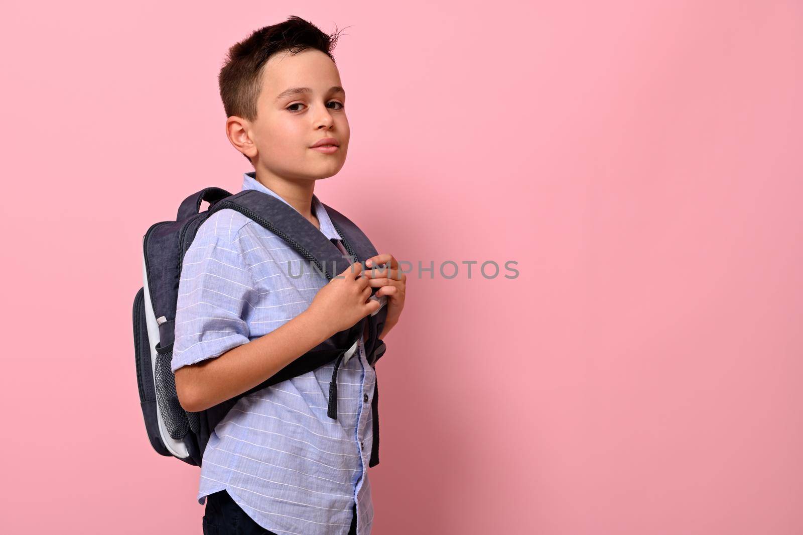 Side portrait of a schoolboy with a school bag on his back on pink background with copy space. Back to school concepts by artgf