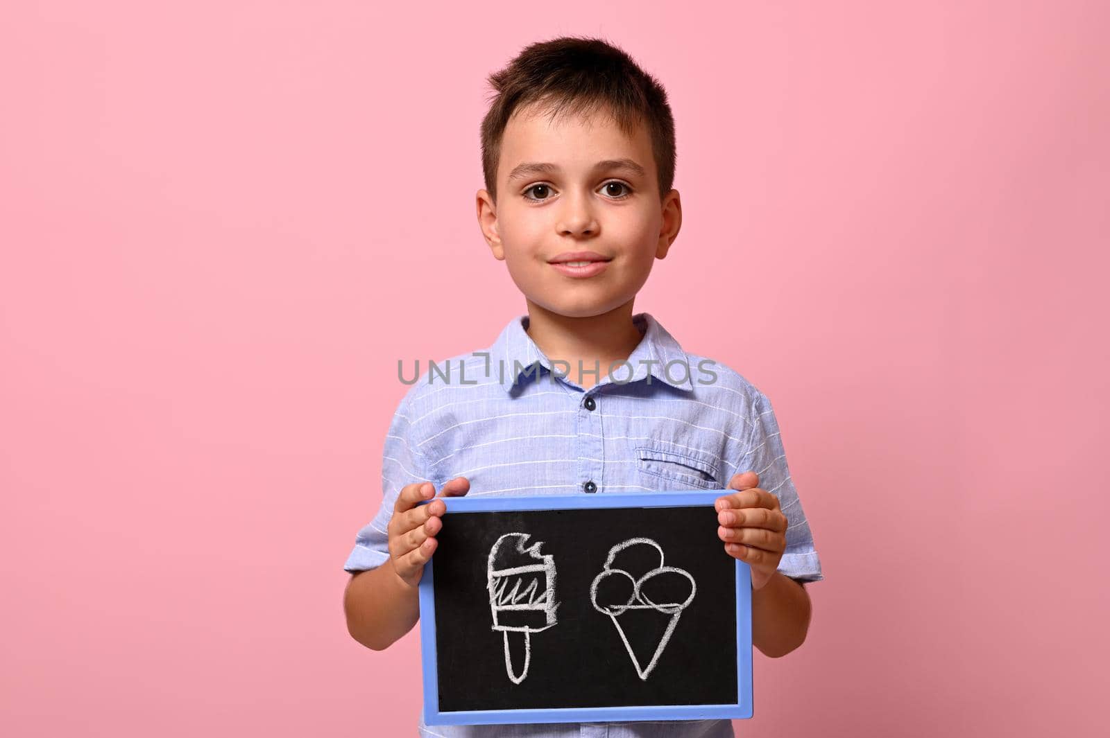 Isolated portrait on pink background of a handsome schoolboy holding a blackboard with drawn ice cream. by artgf