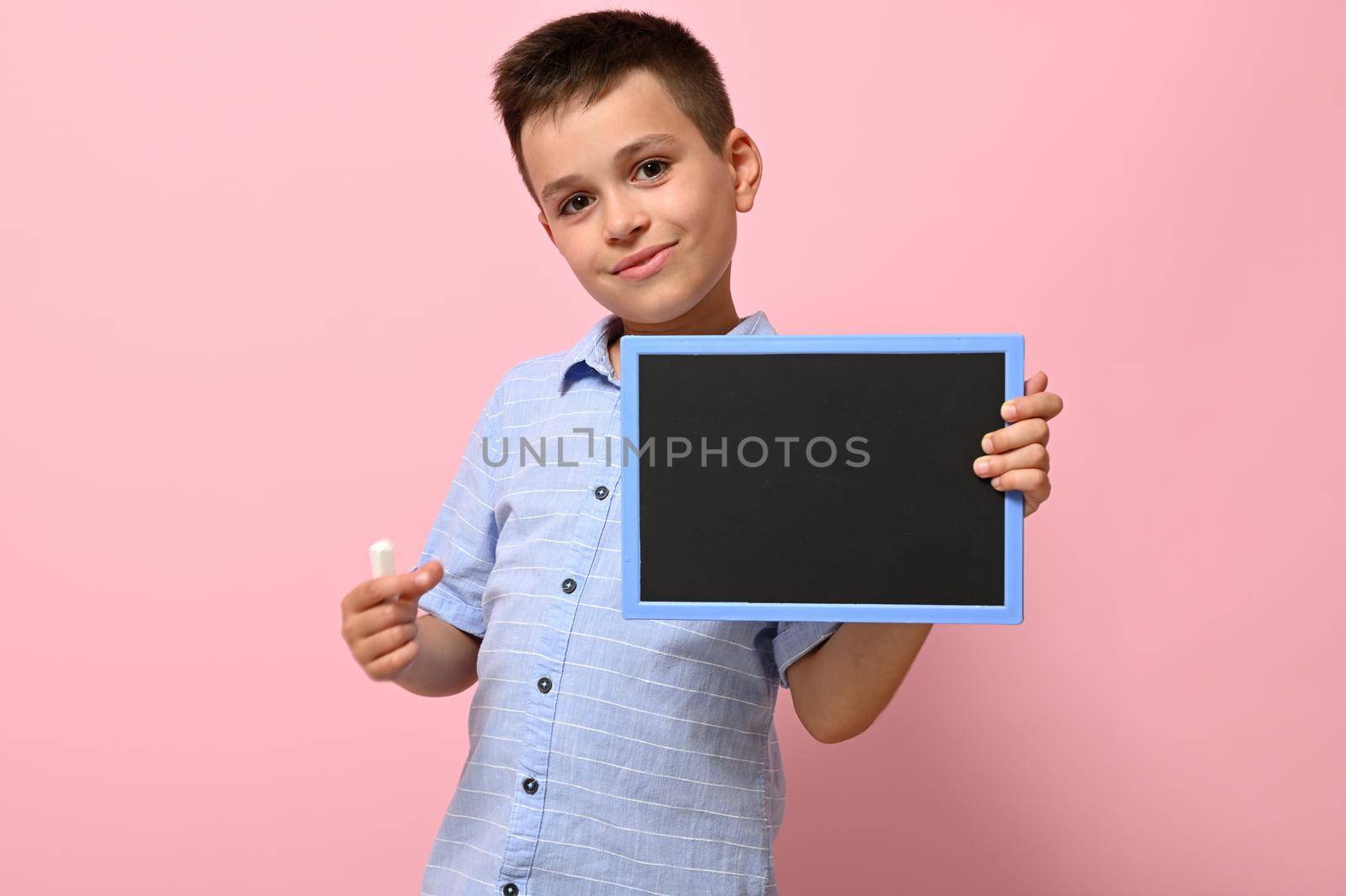 Isolated portrait on pink background of a schoolboy with chalk and chalkboard in his hands. Back to school. Concepts by artgf