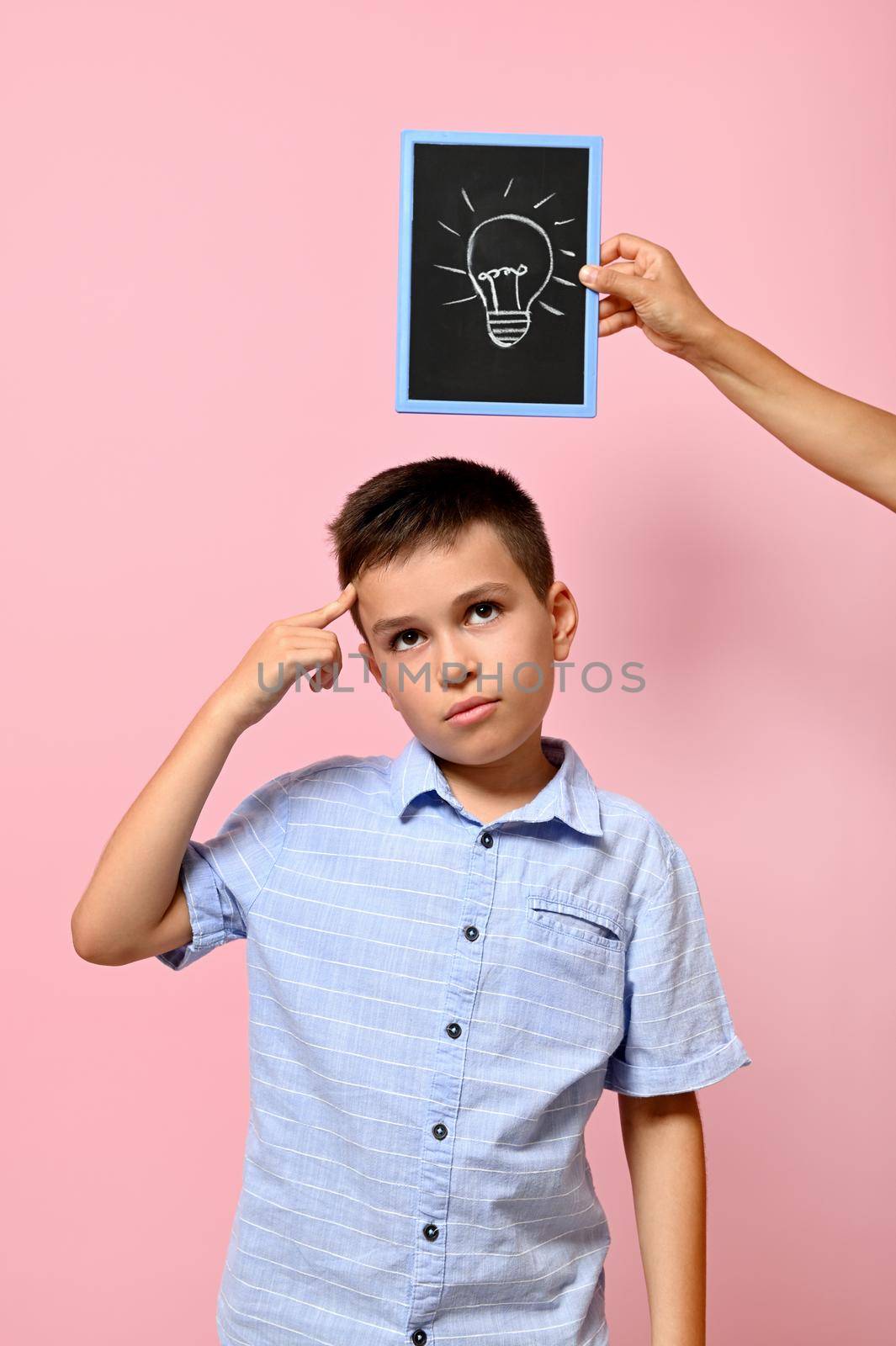 Chalkboard with drawn lamp, idea symbol, and schoolboy looking pensively with forefinger on temple, isolated on pink background with copy space. Concepts. by artgf