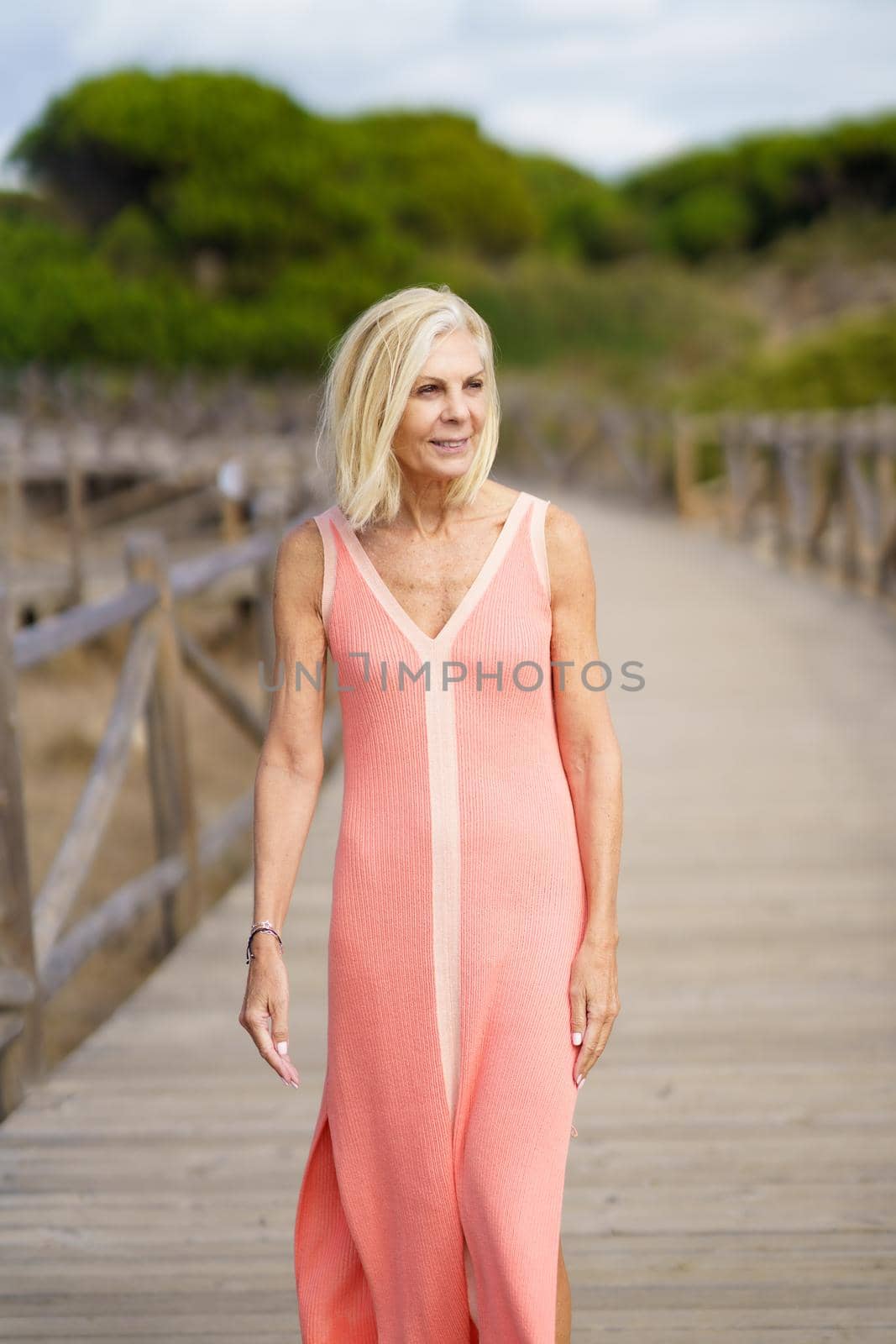 Beautiful mature female walking along a wooden path near the beach., wearing a nice orange dress. Elderly woman enjoying her retirement at a seaside retreat.