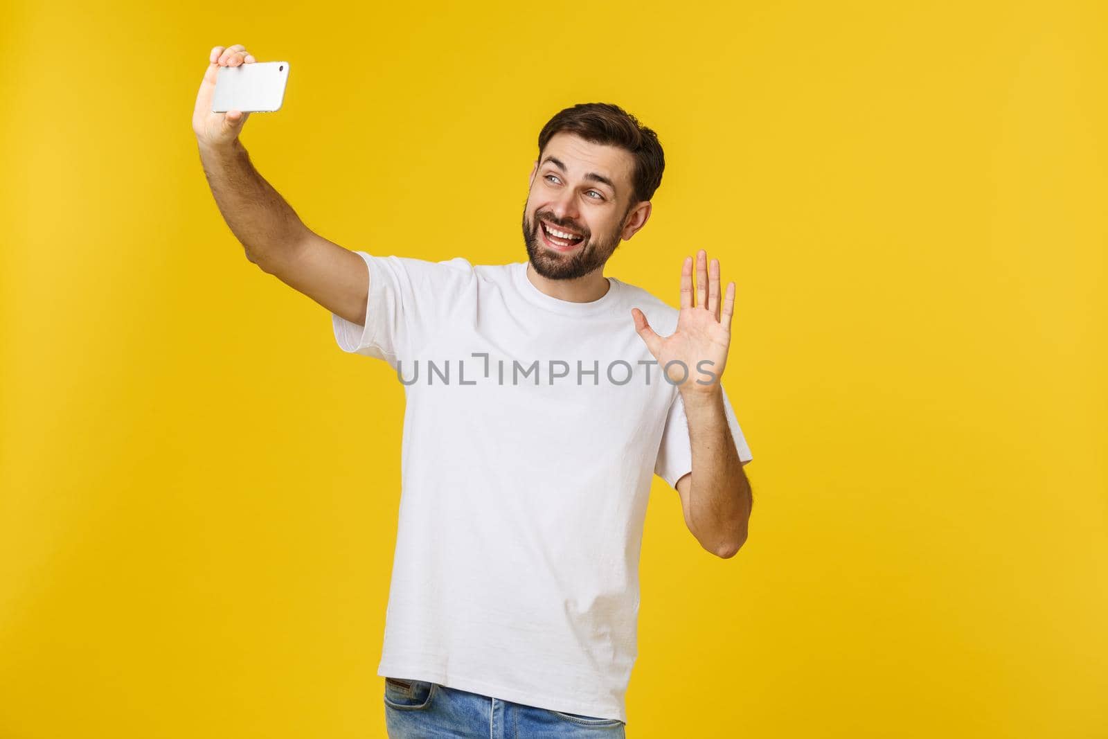 Closeup of young handsome man looking at smartphone and taking selfie. isolate over yellow background