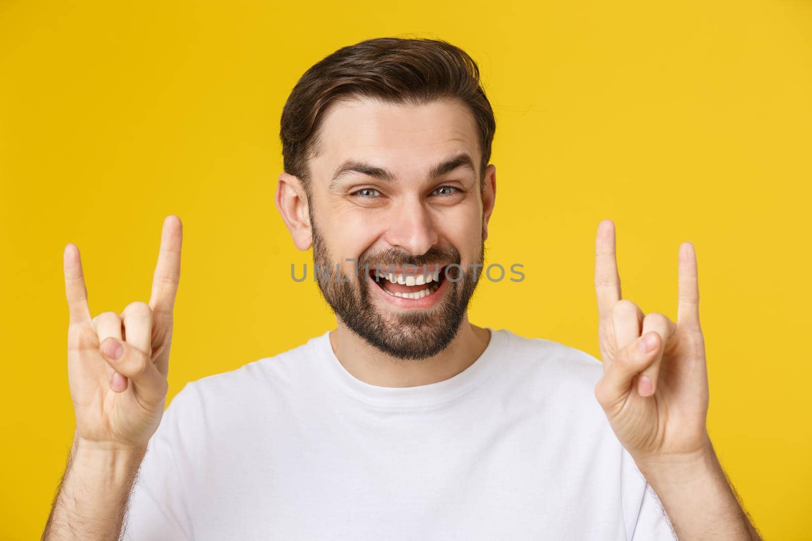 Young caucasian man wearing casual white t-shirt over yellow isolated background shouting with crazy expression doing rock symbol with hands up. by Benzoix