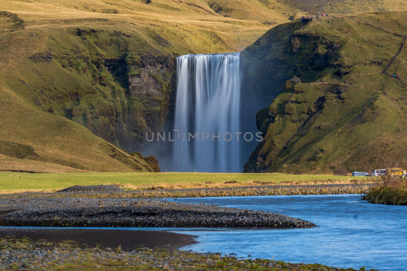 Long exposure of Skogafoss waterfall in Iceland from the distance with tourists hiking and blurred cars